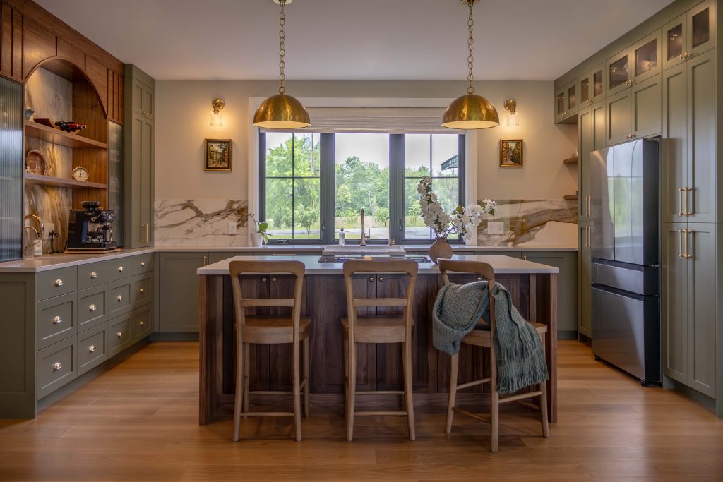Wide-angle view of the Orchard Hill Kitchen featuring mossy green shaker cabinets, a central walnut island, and fluted glass uppers.
